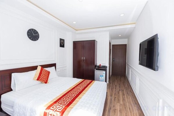 Une chambre d’hôtel avec un lit, une horloge, une armoire, un téléviseur et un couloir.