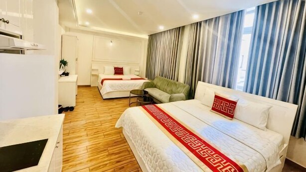 Quarto de hotel com uma cama grande, uma cama menor, um sofá, uma escrivaninha e uma cozinha compacta.