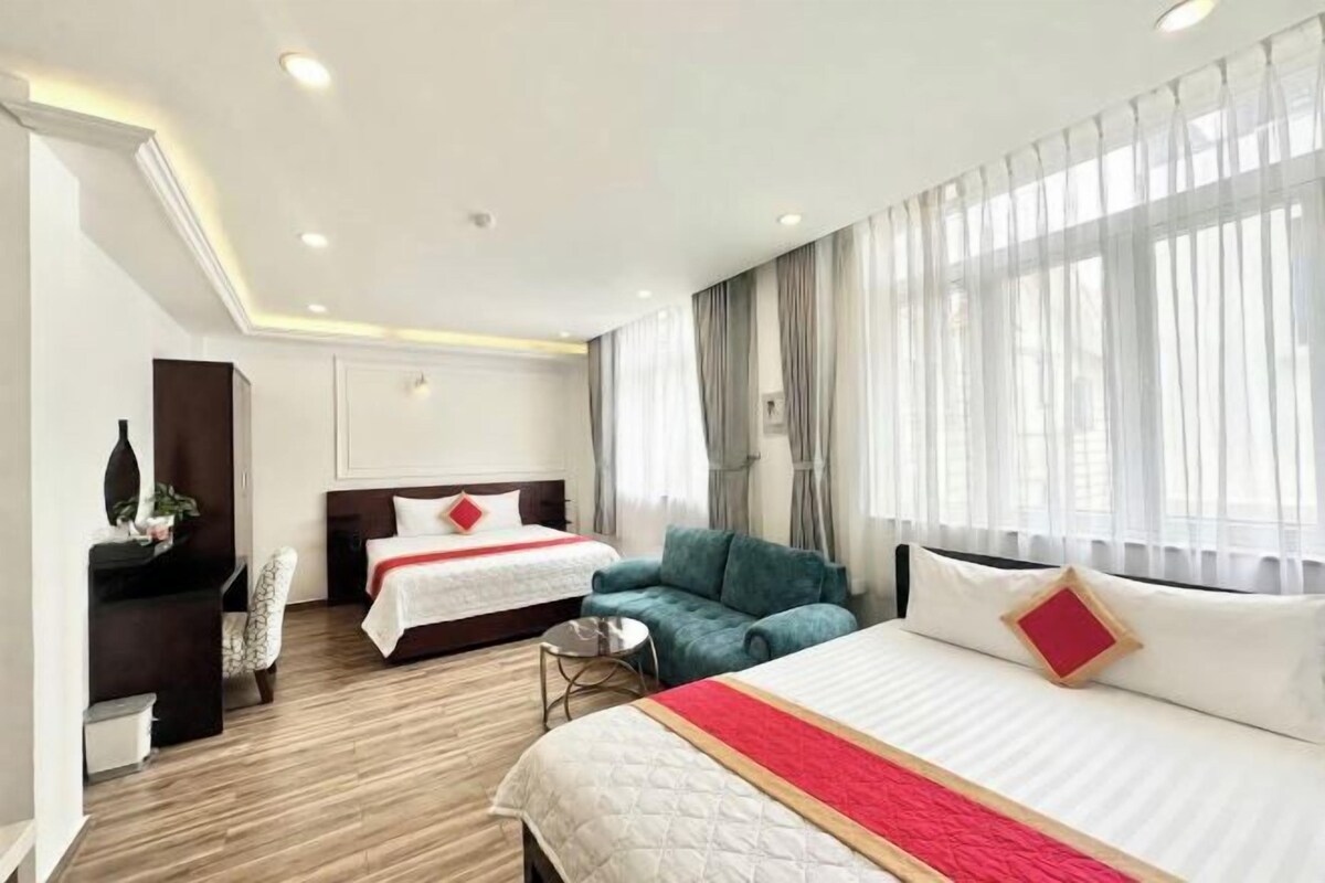 A hotel room with a large bed, a smaller bed, a sofa, a desk, and a chair.