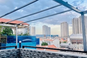 Blick auf eine Stadtlandschaft von einem Balkon mit Metallgeländer, hohen Gebäuden und einer blauen Wand.