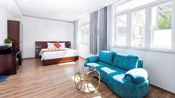 A hotel room with a bed, a blue sofa, a small round table, and large windows. - Phu Gia Hotel 99-101 Him Lam (Ho Chi Minh City)
