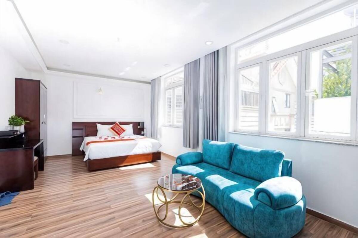 Ein Hotelzimmer mit einem Bett, einem blauen Sofa, einem kleinen runden Tisch und großen Fenstern.