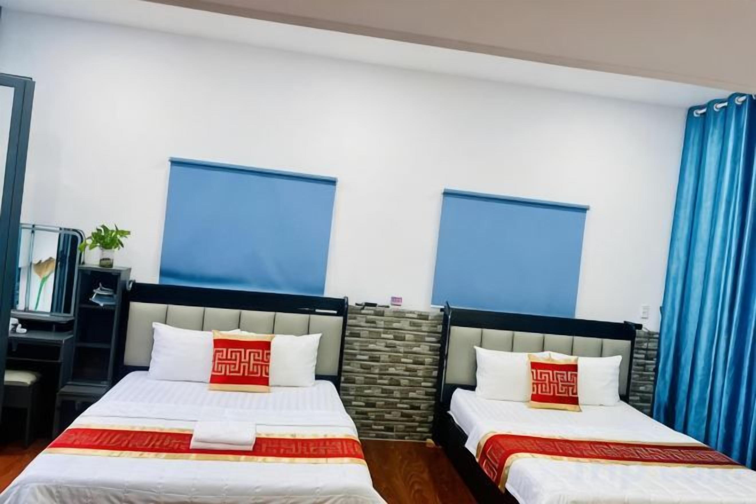 A hotel room with two beds, a desk, and a window with blue curtains.