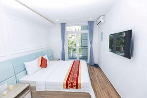 Hotellihuone, jossa on sänky, yöpöytä, ikkuna verhoilla ja seinälle asennettu televisio.