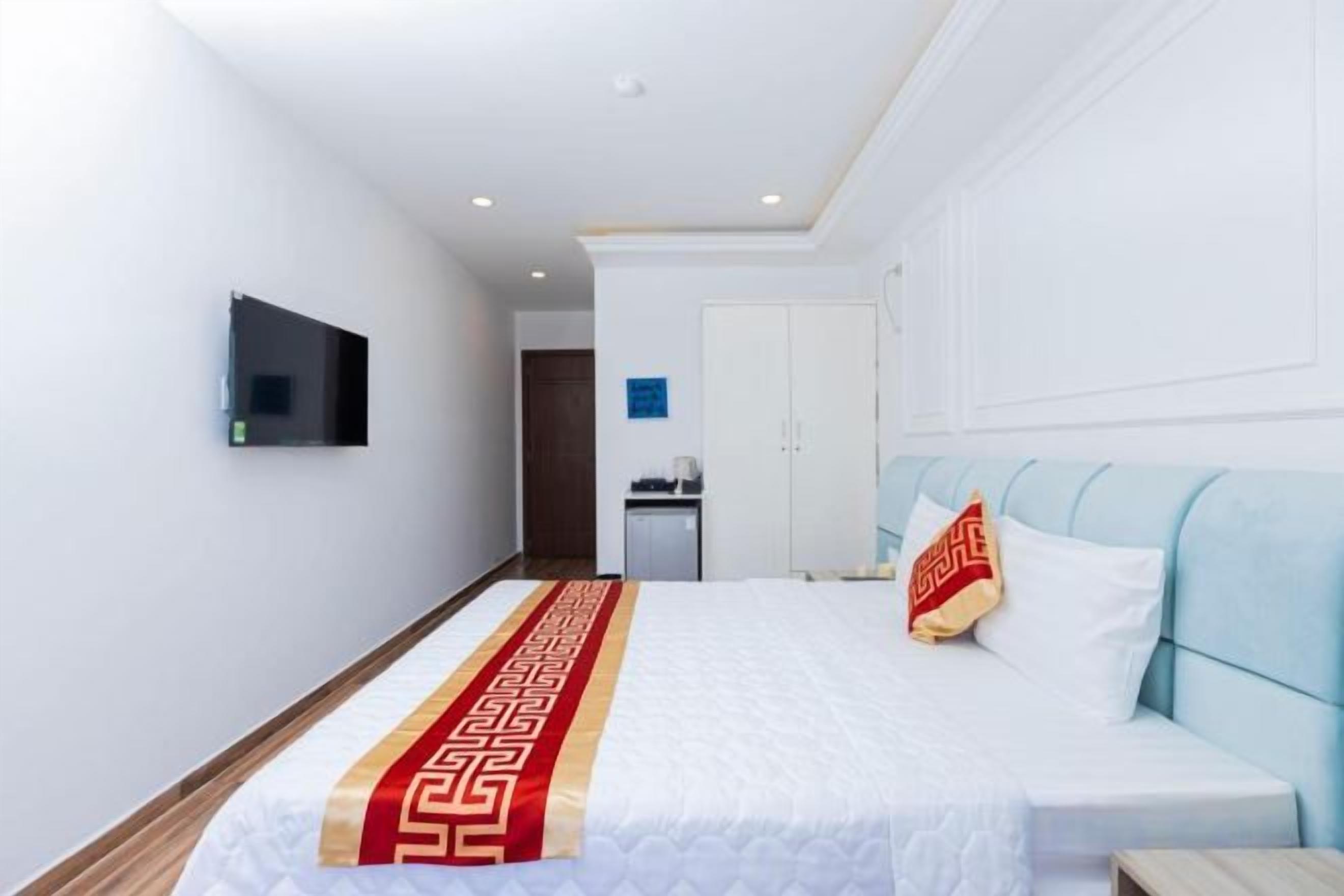Quarto de hotel com uma cama, televisão na parede e uma pequena mesa com cadeira.