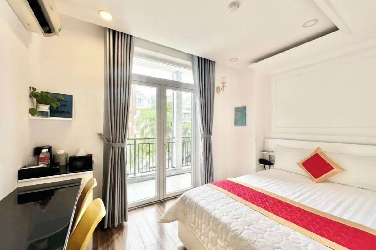 A hotel room with a bed, a desk, a chair, a window with curtains, and a balcony.