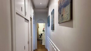 Een gang met witte muren, houten vloeren en een plafond met inbouwverlichting. Links bevinden zich deuren en rechts kunstwerken.