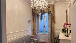 Een kamer met een bank, een kroonluchter, een raam met gordijnen en een spiegel.