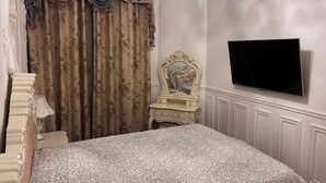 Een slaapkamer met een bed, een televisie, een kaptafel en gordijnen.