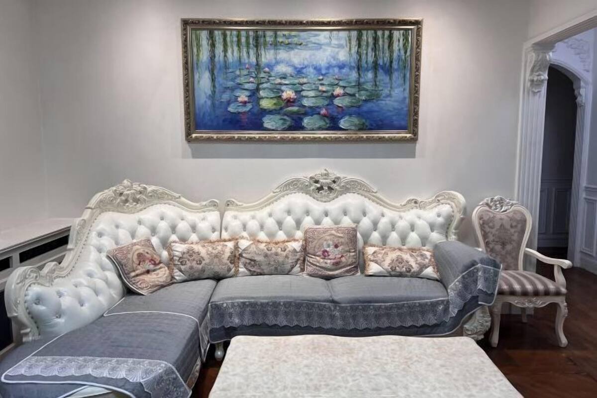 Een klassieke, witte gestoffeerde bank met decoratieve details, een bijpassende fauteuil en een decoratief schilderij van een vijver met waterlelies.