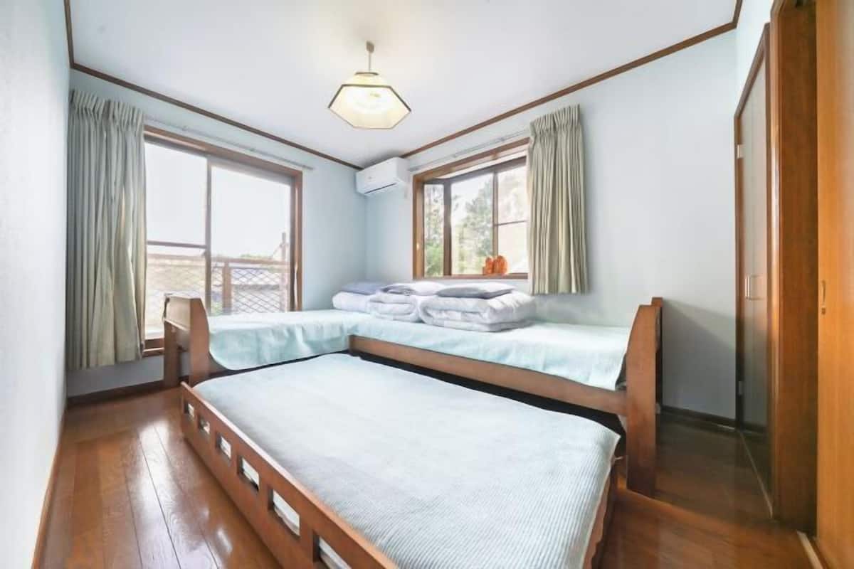 A bedroom with a bunk bed, two windows with curtains, a wooden floor, and a ceiling light fixture.