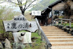 Une enseigne en bois ornée de caractères japonais, un escalier menant à un bâtiment et un arbre au premier plan.
