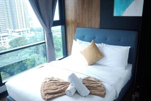 Habitación de hotel con un ventanal grande, cama con ropa de cama blanca, cabecera azul y vista a un paisaje urbano.