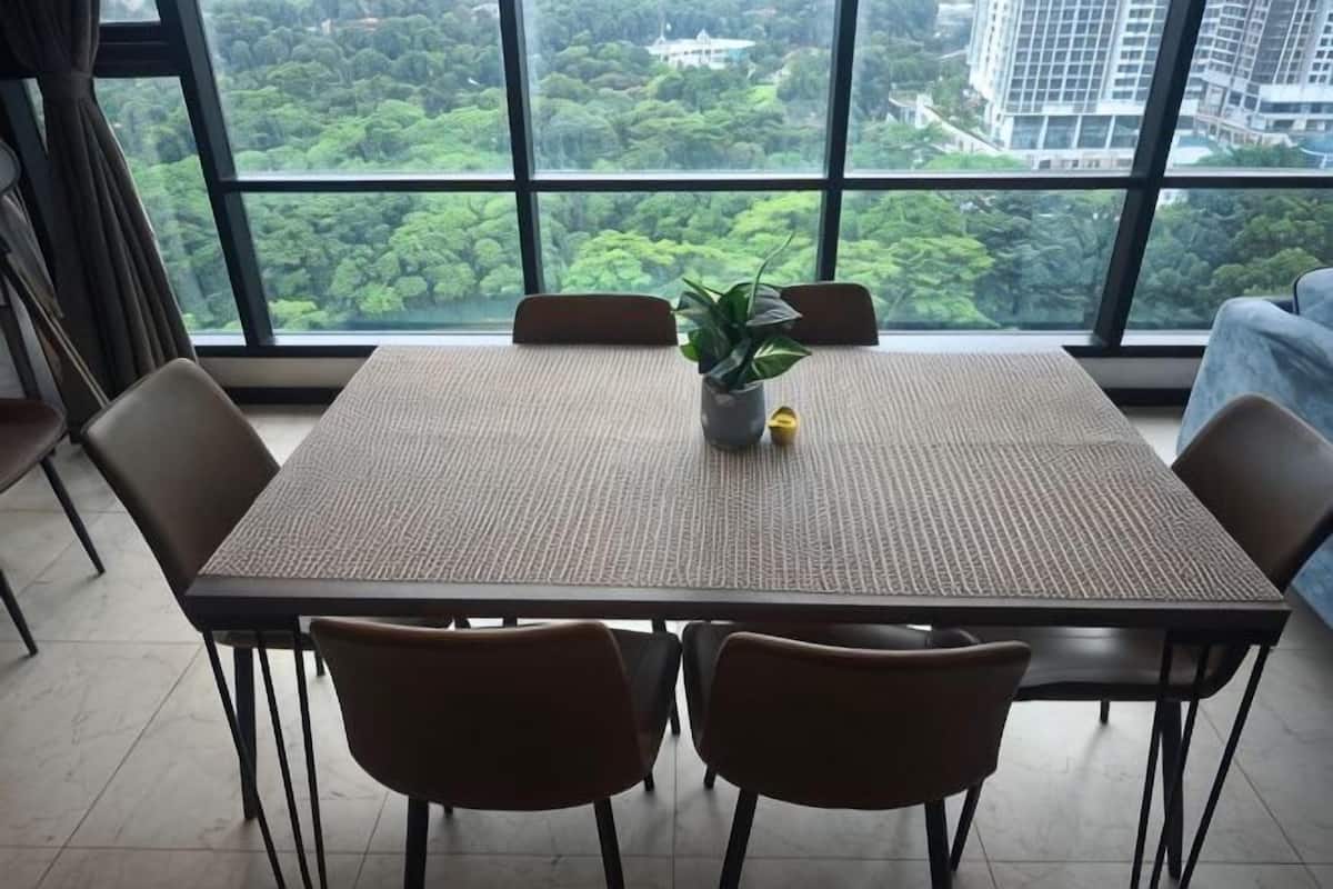 Una mesa con cuatro sillas, una planta en maceta y vistas a zonas verdes a través de amplios ventanales.
