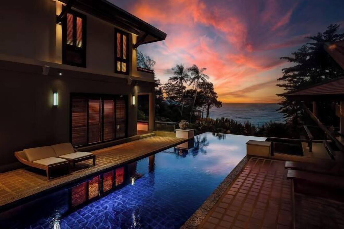 Ein modernes Haus mit Swimmingpool, Terrasse und Blick auf den Ozean bei Sonnenuntergang.