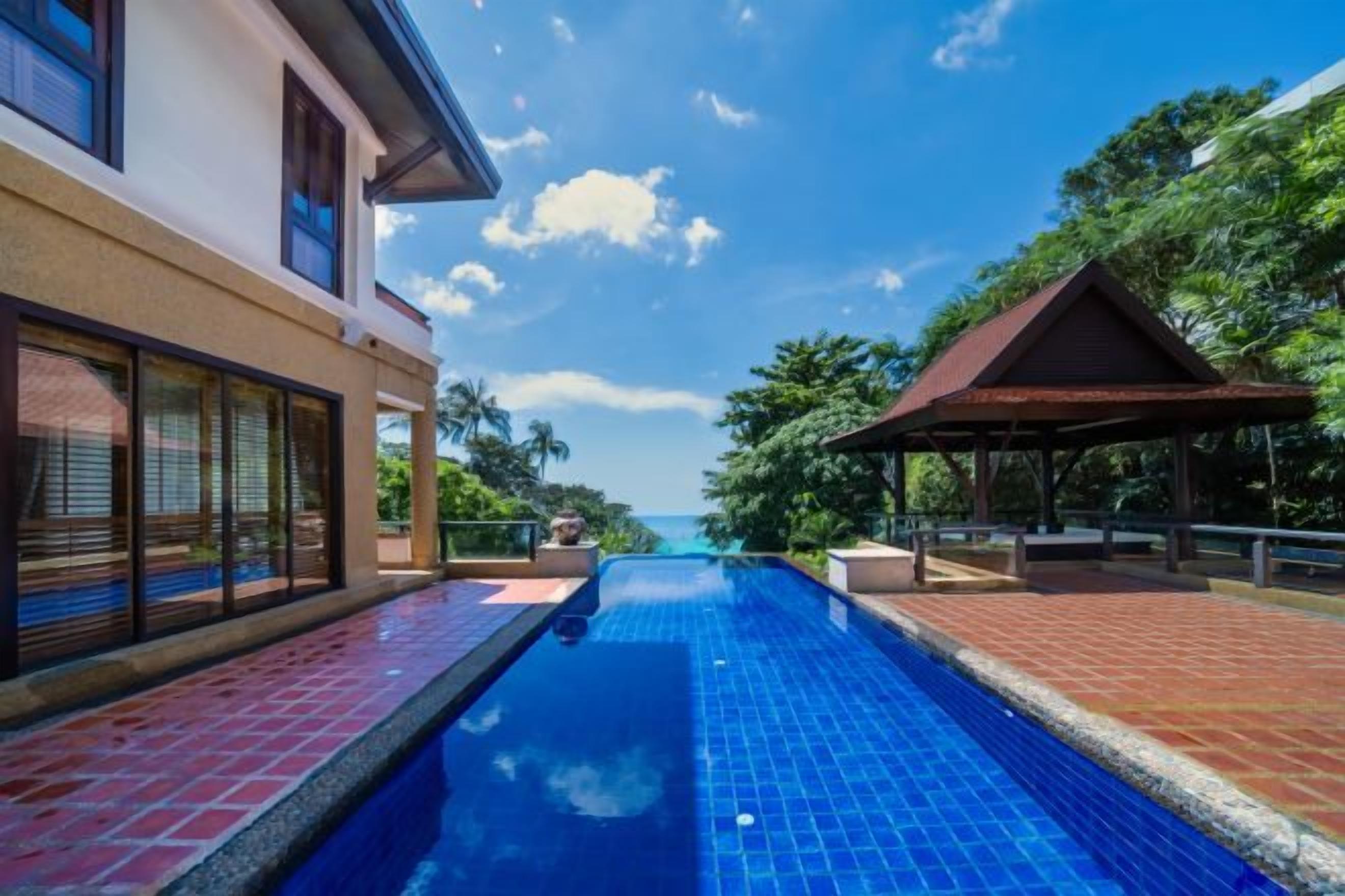 A swimming pool with a clear view of the ocean, a covered seating area, and a building with large windows.
