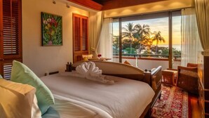 A hotel room with a large bed, a view of palm trees and sunset, wooden beams, and a painting on the wall. - Boutique 5 Bedroom Seaview Pool Villa Kata Beach Phuket Warm Plus (Phuket)