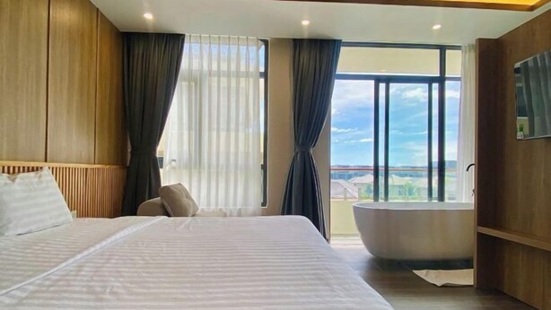 A modern hotel room with a large bed, a bathtub, and a view of the city. - Aurora Bao Anh Hotel (Binh Kien)