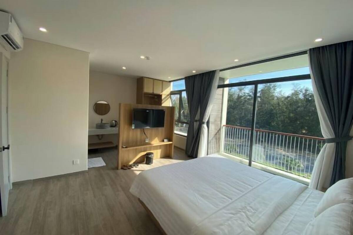 Une chambre avec un grand lit, une télévision, un petit bureau et un balcon avec vue.