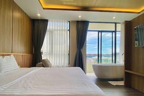 A hotel room with a large bed, a bathtub, and a view of the city.
