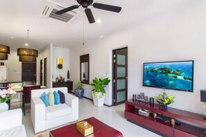 A modern living room with a flat-screen TV, a ceiling fan, and a dining area with a kitchen in the background. - Villa Onyx H4 (Phuket)