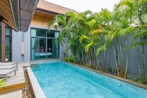 Ein moderner Pool mit klar blauem Wasser, umgeben von einer Holzterrasse und Palmen.