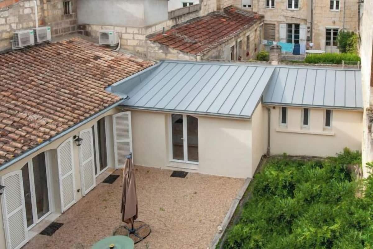 A courtyard with a tiled roof, a small building with a window, and a table with an umbrella.