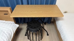 Ein kleiner Holztisch mit einem schwarzen Metallhocker, platziert zwischen zwei Betten in einem Raum mit blauer Vorhangwand.