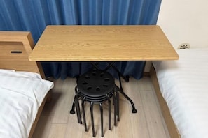 A small wooden table with a black metal stool underneath, positioned between two beds in a room with a blue curtain backdrop. - YMK Oshiage 4B (Tokyo)