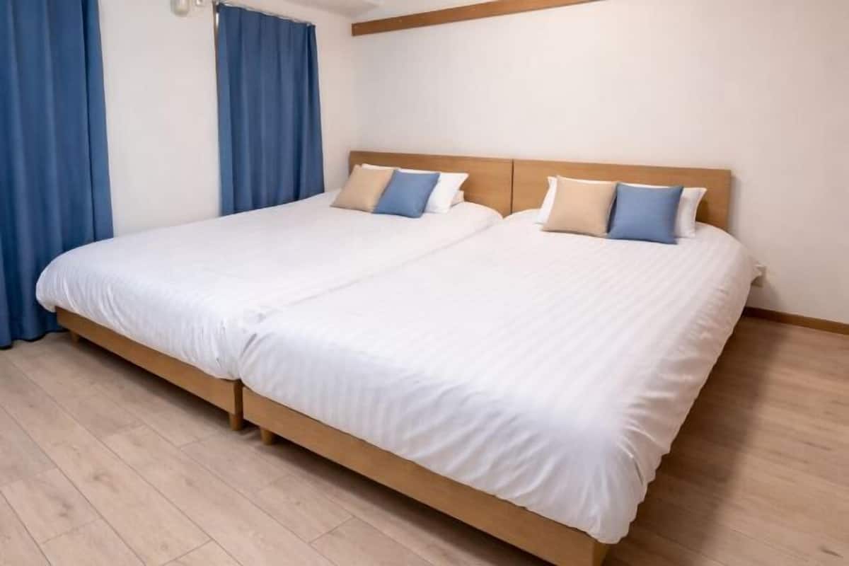 A double bed with a wooden headboard, white bedding, and blue curtains.