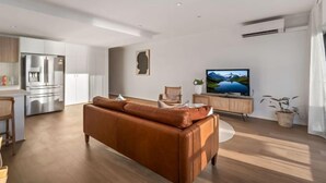 A modern living room with a brown leather sofa, a flat-screen TV, and a wooden cabinet. - Sol Sands: Oceanfront Balcony Henley Beach (Henley Beach)