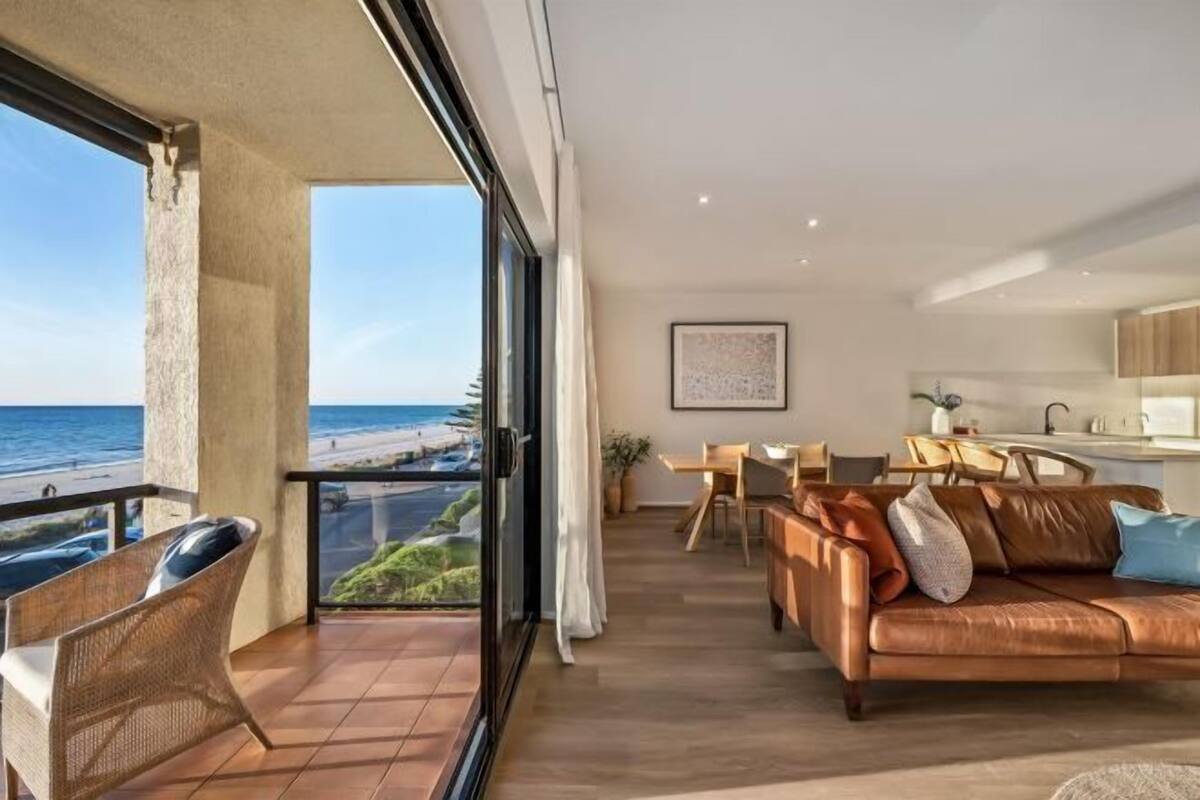 A spacious balcony with a view of the beach, a cozy seating area with a leather sofa, and a minimalist kitchen.