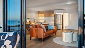 A modern living area with a sofa, a coffee table, and a view of the ocean through large windows. - Sol Sands: Oceanfront Balcony Henley Beach (Henley Beach)