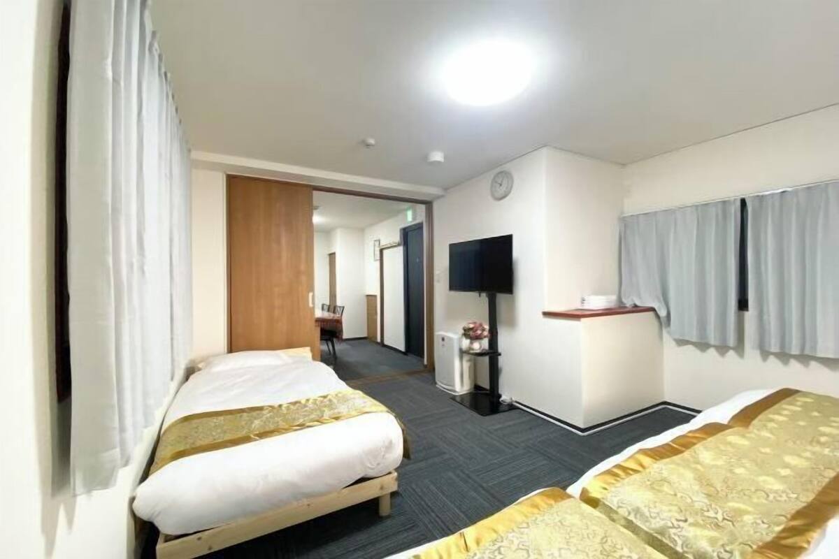 Een hotelkamer met twee bedden, een televisie, een tafeltje en een klok aan de muur.