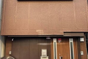 A brown textured wall with a door and a small sign above it. - Asakusa MASAKAZU House 1F2F (Tokyo)