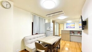 Un espace de vie compact comprenant un canapé, une table à manger, des chaises, une horloge, un appareil de climatisation, un téléviseur et un coin cuisine.