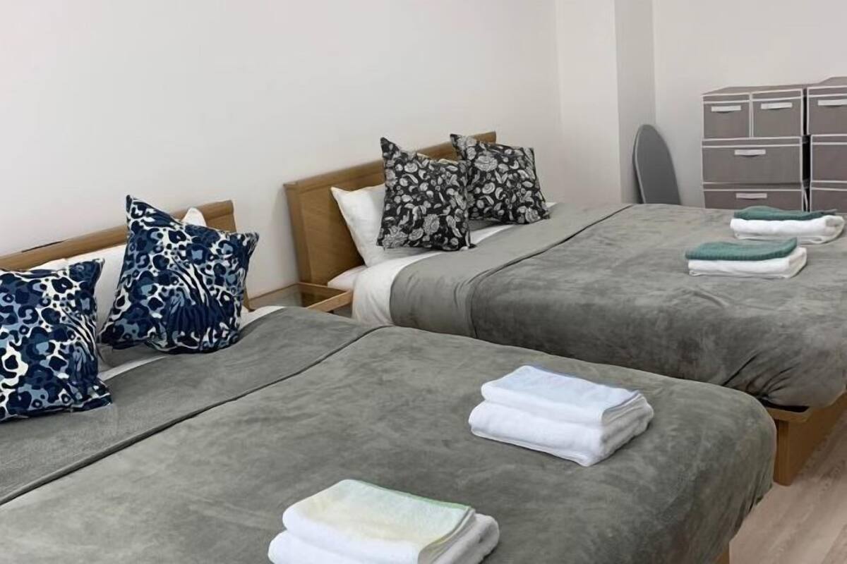 Habitación de hotel con dos camas, ropa de cama gris, almohadas estampadas y toallas dobladas con cuidado.
