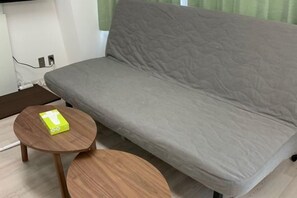 A grey sofa with a wooden side table and a small round table with a green object on it. - Shin-Osaka 1005 (Osaka)