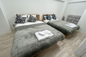 A hotel room with two beds, grey bedding, white pillows, a grey blanket, and neatly folded white towels.