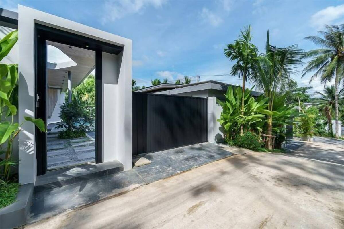 Uma casa moderna com calçada de concreto, rodeada por vegetação tropical.