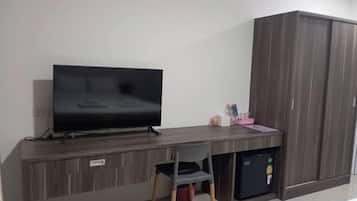 Une chambre dotée d’un téléviseur à écran plat posé sur un bureau en bois, d’une chaise, d’un petit réfrigérateur et d’une armoire.