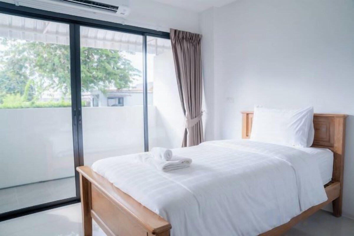 A hotel room with a bed, a sliding glass door to a balcony, and a curtain.
