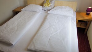 A double bed with white linens and a decorative pillow, a wooden nightstand with a lamp, and a red carpeted floor. - Hotel Rosenhof am Main (Offenbach am Main)