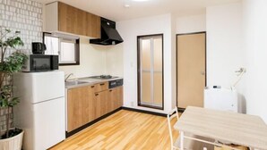 A compact kitchen with a microwave, stove, and sink, wooden cabinets, and a potted plant. - Sparrow Color · Fangnan (Tokyo)