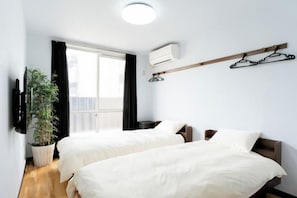 Ett hotellrum med två sängar, en krukväxt, ett fönster med gardiner och en väggmonterad luftkonditioneringsanläggning.
