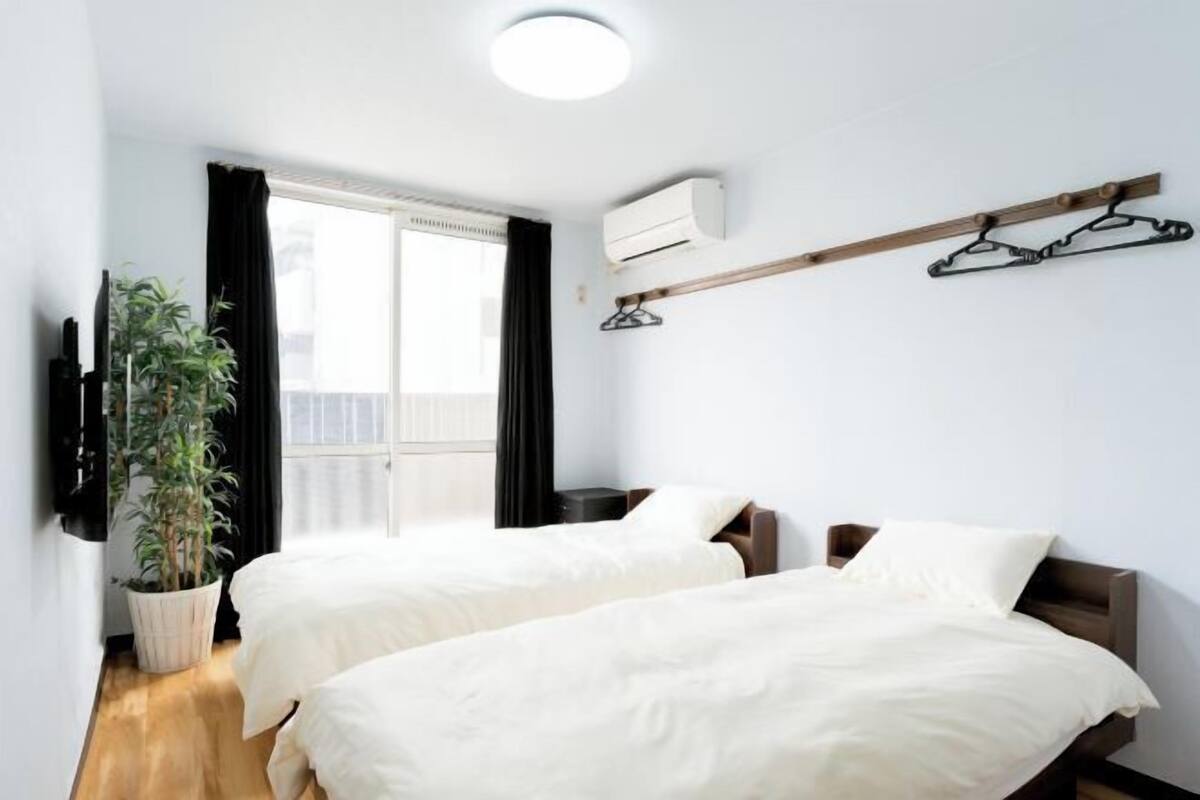 Una habitación con dos camas, una planta en maceta, un televisor y una ventana con cortinas.