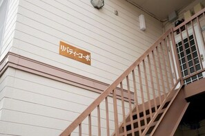 Eine Treppe mit Handlauf führt zu einer Tür mit Fenster. Ein Schild mit japanischen Schriftzeichen ist an der Wand sichtbar.
