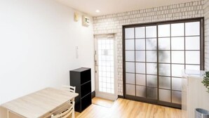 A room with a sliding glass door, a wooden table, a black storage unit, and a white wall with a small picture. - Sparrow Color · Fangnan (Tokyo)