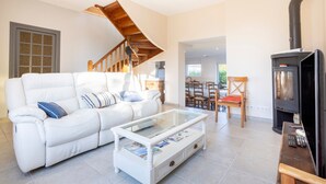 Ein Wohnzimmer mit weißem Sofa, einem Glastisch, einer Holztreppe und einem Kaminofen.