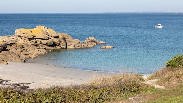 Eine Küstenlandschaft mit Felsformationen, einem Sandstrand und einem Boot auf dem Wasser.